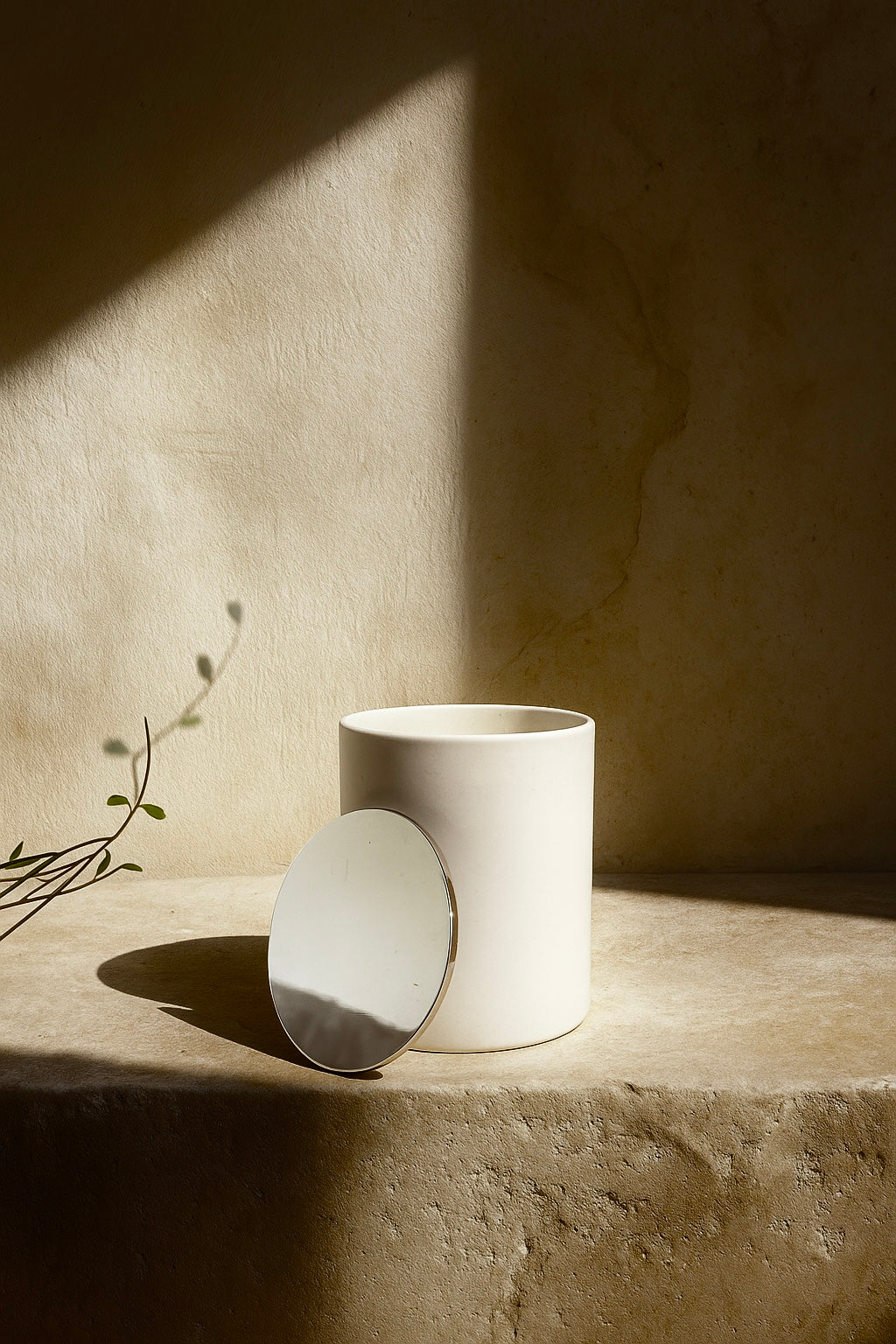 White ceramic container with a lid on a stone surface against a beige wall luxury winter candle UK with birch, smoky peat, patchouli, and amber. A premium scented candle for calming winter home fragrance and cozy ambiance.