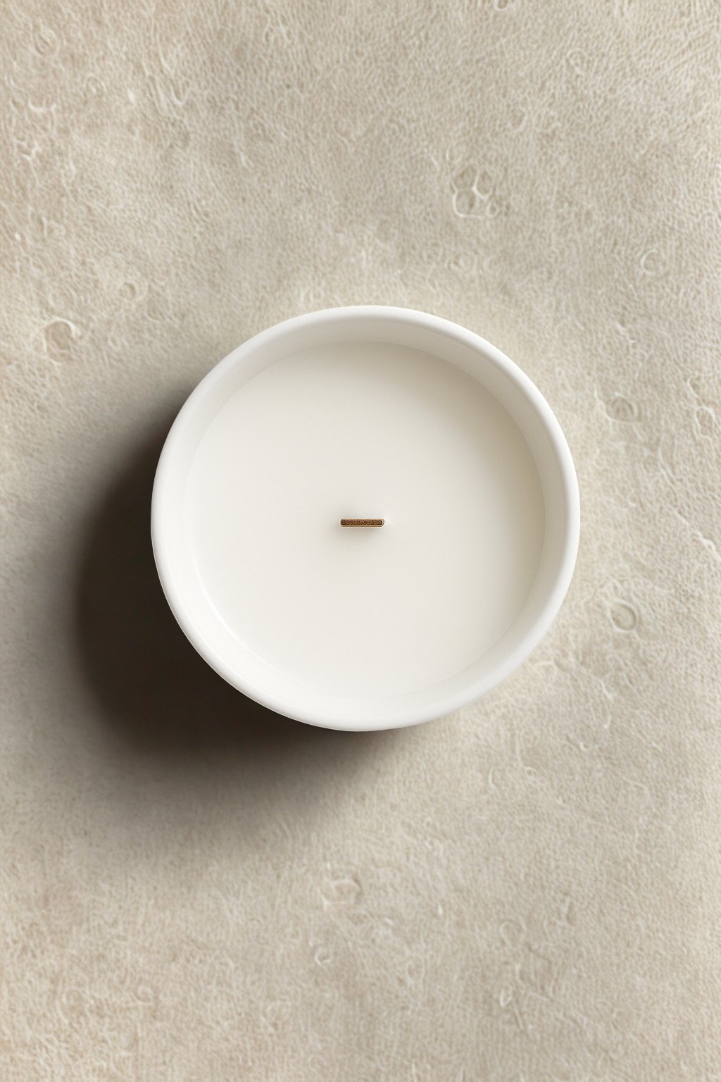 White candle in a ceramic holder on a beige surfaceLuxury winter candle UK with birch, smoky peat, patchouli, and amber. A premium scented candle for calming winter home fragrance and cozy ambiance.