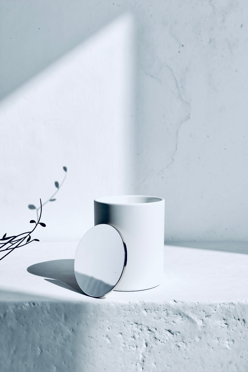 White ceramic cup on a light grey surface with a minimalistic backgroundLuminous snow front side ,luxury winter candle“ Aurum Blanc luxury winter candle in minimalist white vessel, premium scented candle with white amber and woody notes.”