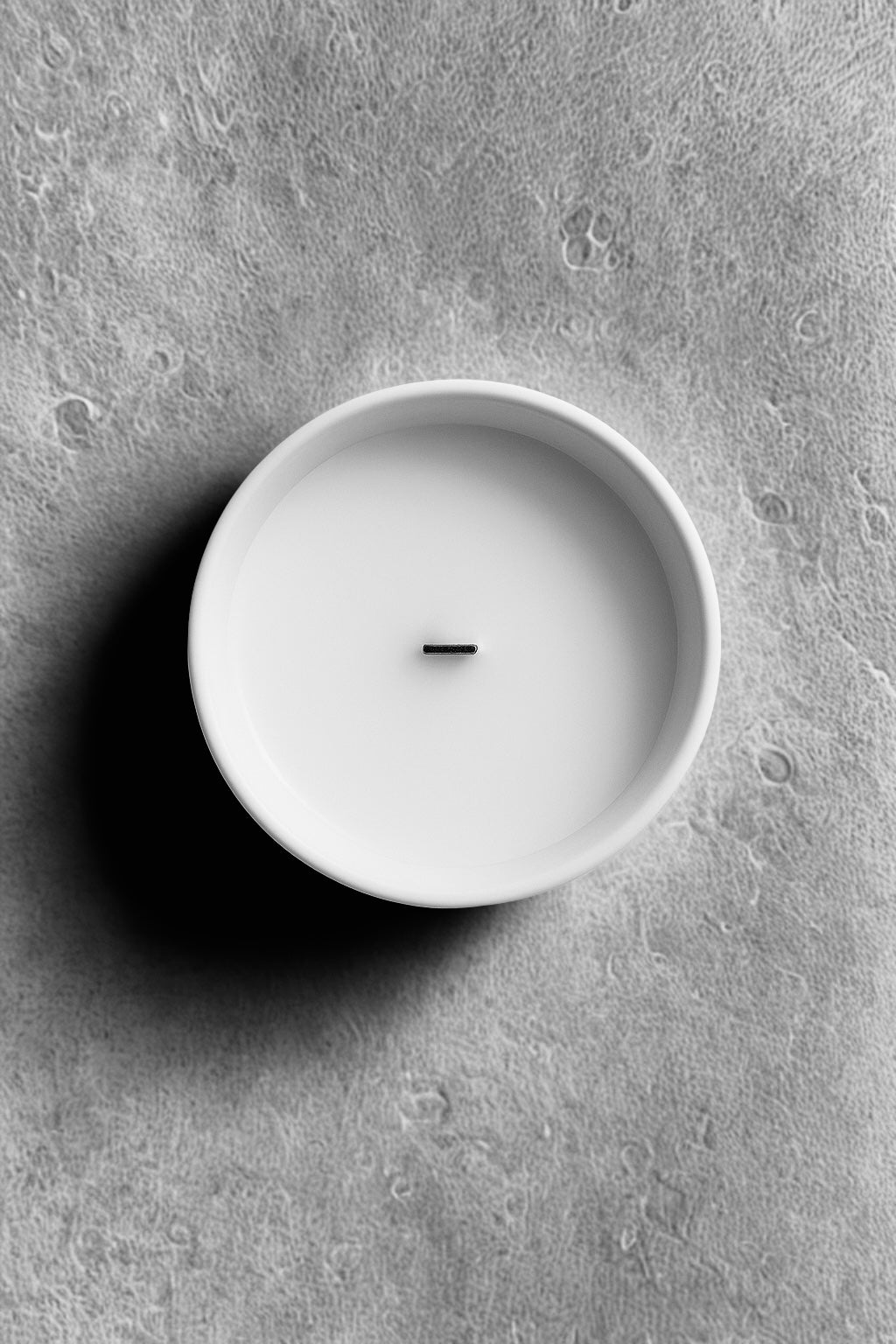 White candle in a white holder on a grey concrete surface Aurum Blanc Nuit d’Hiver luxury winter candle UK in white ceramic vessel with silver lid, premium scented candle with eucalyptus, cedar, patchouli, and amber notes.