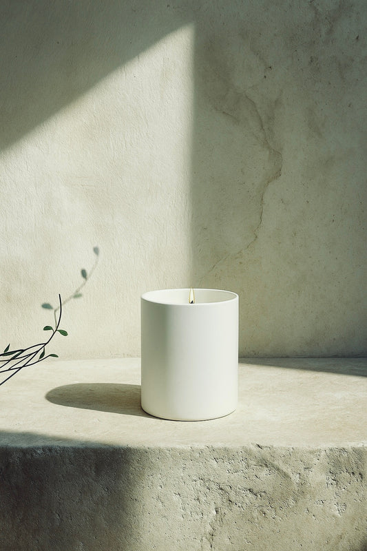 White candle on a concrete surface with a neutral background“Aurum Blanc Éclat de Noël luxury winter candle UK in white ceramic vessel with silver lid, premium scented candle with orange, cinnamon, clove and almond notes for warm winter home fragrance.”